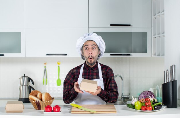 Front view of puzzled male chef holding box in the kitchen