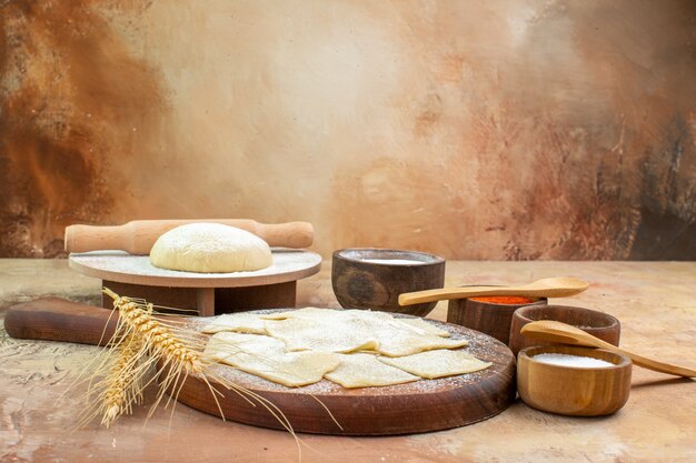 Front view raw dough slices with flour and seasonings on a cream desk