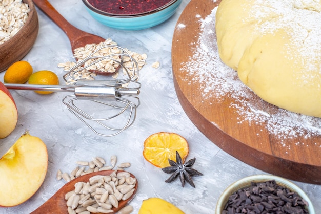 Front view of raw pastry flour on round wooden board grater hazelnuts fresh fruits chocolates on gray background