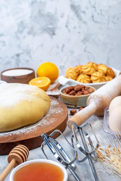 Front view of raw pastry on wooden round board and set of various foods grater on ice background