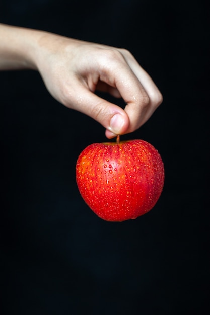 Front view of red apple in hand on dark surface