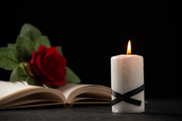 Front view of red rose with book and candle on black