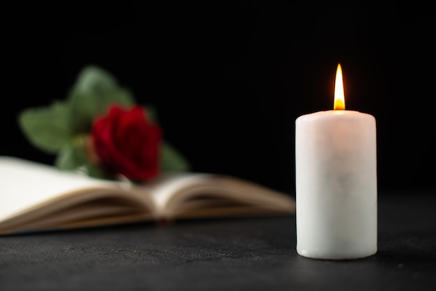 Front view of red rose with open book and candle on black