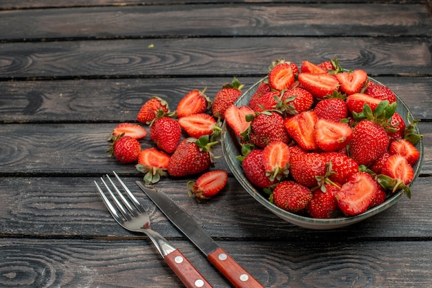 Front view red strawberries sliced and whole fruits on a dark wooden rustic desk summer color tree  juice berry wild