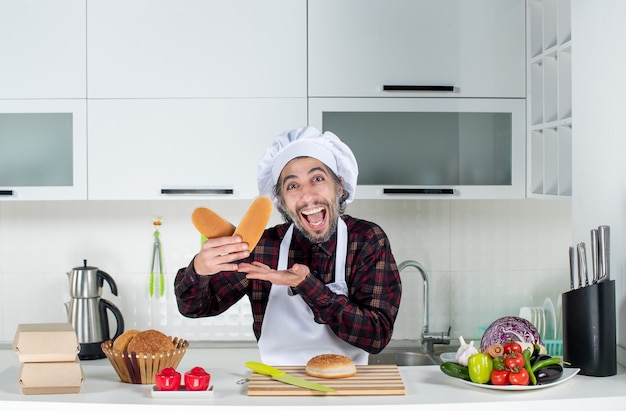 Front view of rejoiced male chef holding bread in the kitchen