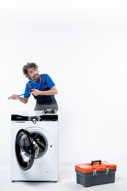 Front view of repairman holding stethoscope with both hands standing behind washer on white wall