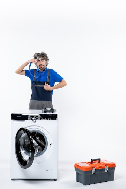 Free photo front view of repairman putting stethoscope to his forehead standing behind washer on white wall