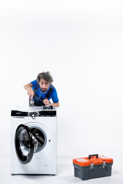 Front view of repairman putting stethoscope over washer on white wall