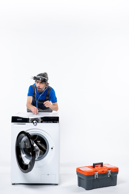 Free photo front view of repairman with head lantern using stethoscope standing behind washer on white wall