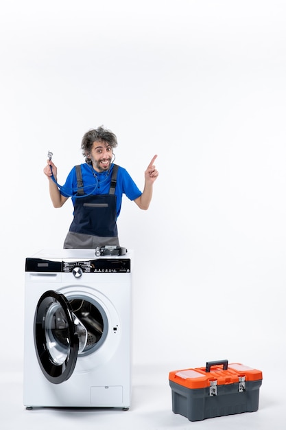 Front view of repairman with stethoscope standing behind washer pointing at right on white wall