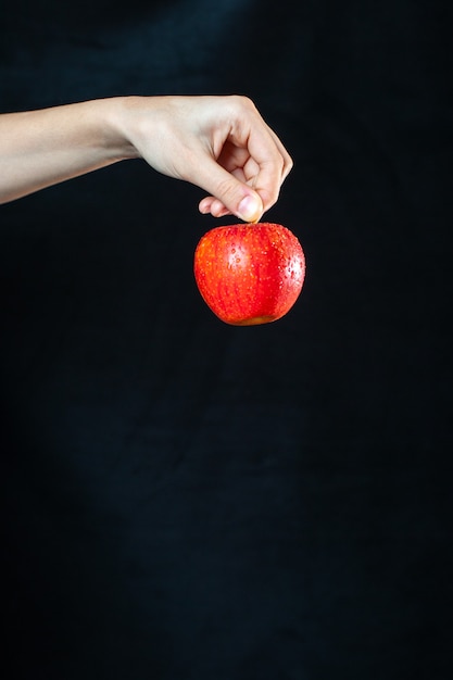 Front view ripe red apple in hand on dark surface