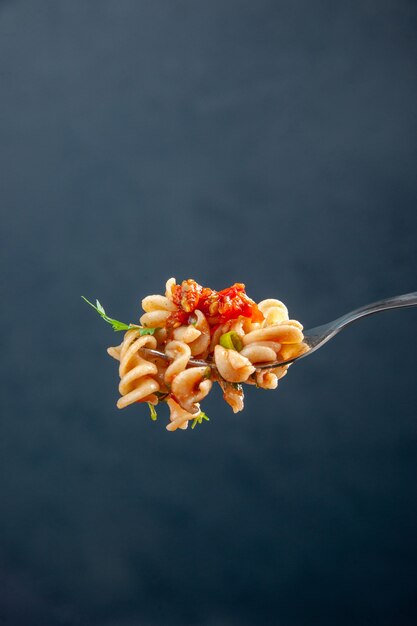 Front view rotini pasta on fork on dark isolated surface free space