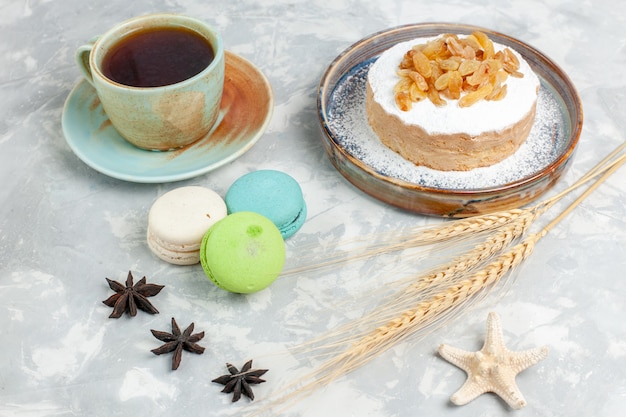 Free Photo front view round little cake sugar powdered with raisins tea and french macarons on white surface sugar sweet biscuit cream pie