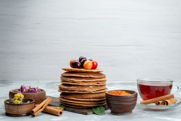 A front view round pancakes baked and delicious with cherries cinnamon and tea on the light desk cake fruit 