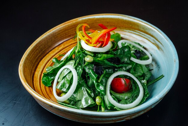 Front view salad of greens with onions tomatoes and bell peppers on a plate