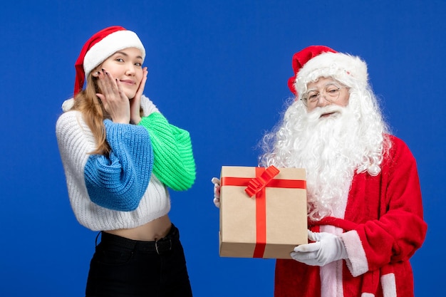 Front view of santa claus along with young female holding present on a blue wall