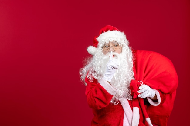 Front view santa claus carrying bag full of presents asking to keep silence on red emotion new year