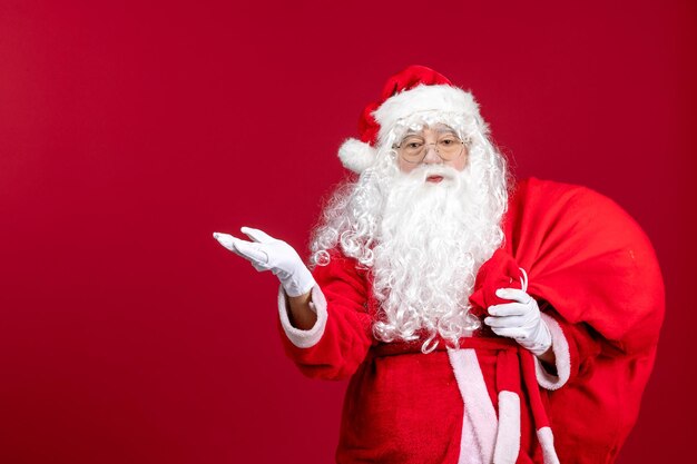 Front view santa claus carrying red bag full of presents on a red christmas emotion new year holiday