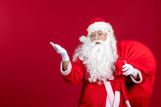 Front view santa claus carrying red bag full of presents on red emotion new year christmas holidays