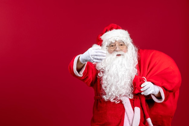 Front view santa claus carrying red bag full of presents on red floor emotion new year christmas