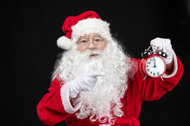 Free photo front view santa claus in classic red suit holding clocks