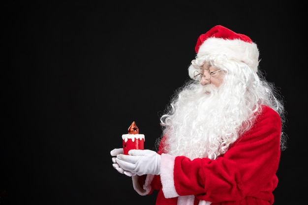 Free photo front view santa claus in classic red suit holding holiday candle