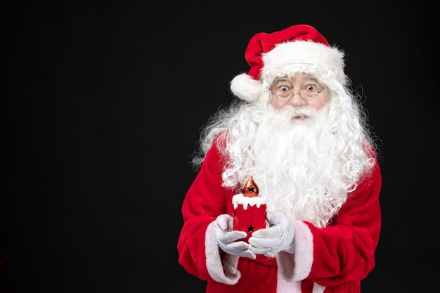 Free photo front view santa claus in classic red suit holding holiday candle