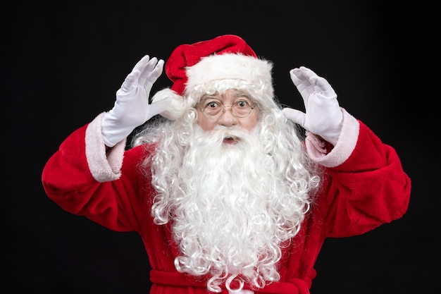 Front view of santa claus in classic red suit with white beard on black wall