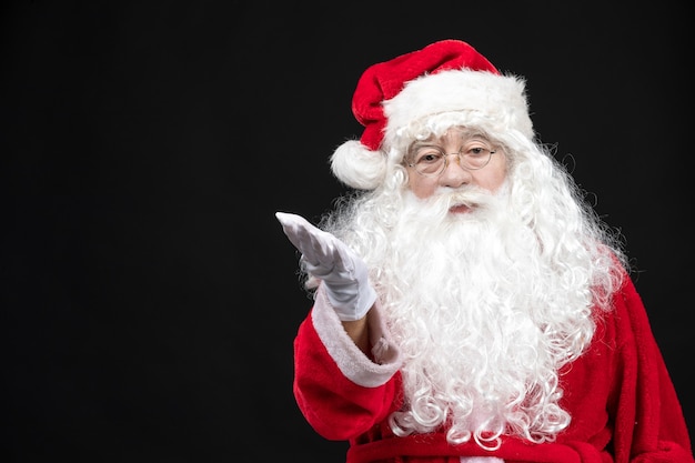 Front view of santa claus in classic red suit with white beard on black wall