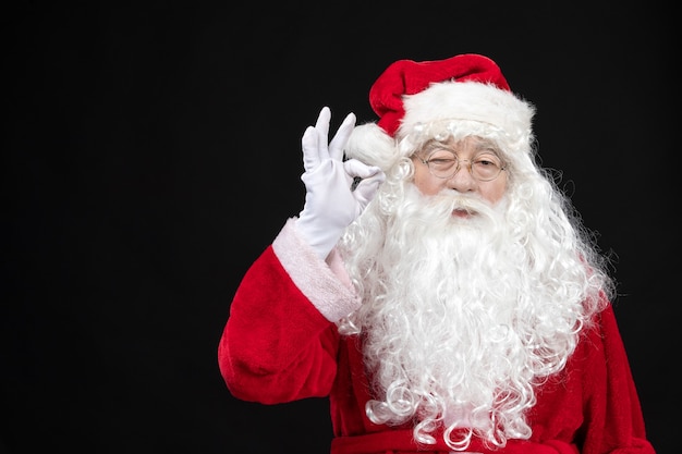 Front view of santa claus in classic red suit with white beard on the black wall