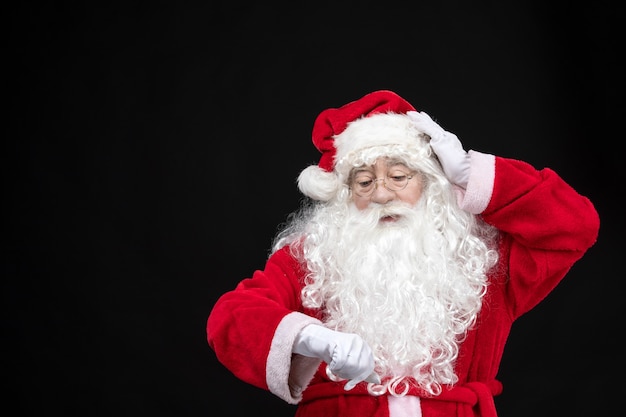 Free photo front view santa claus in classic red suit with white beard checking time