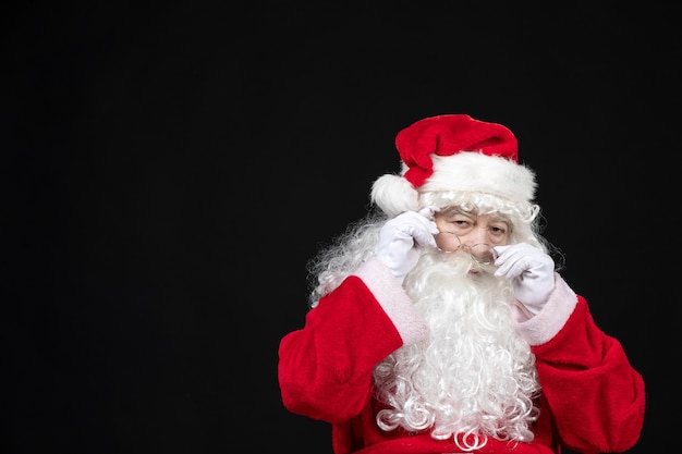 Free Photo front view of santa claus in classic red suit with white beard standing on a black wall