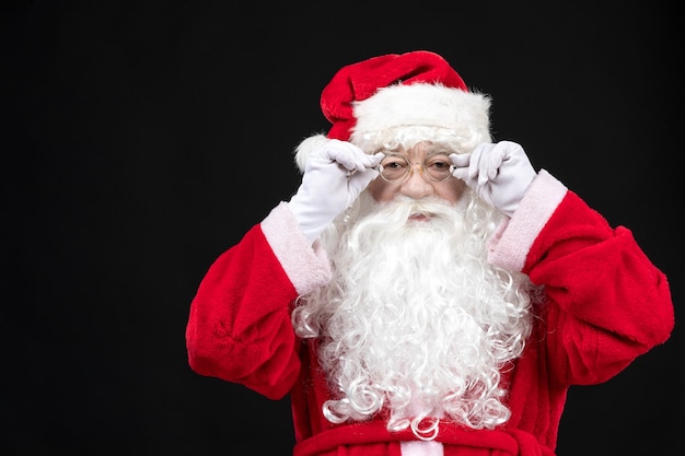 Free Photo front view of santa claus in classic red suit with white beard standing on the black wall