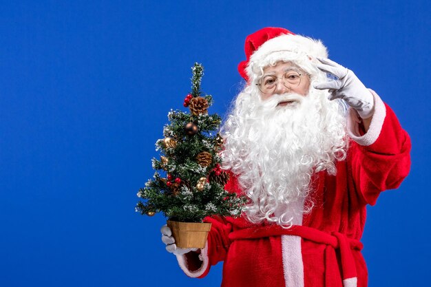 Front view santa claus holding little new year tree on blue christmas new year