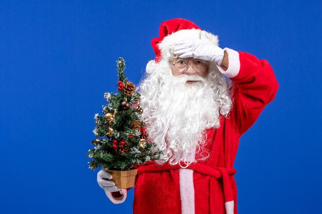 Front view santa claus holding little new year tree on the blue snow christmas new year color