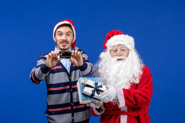 Front view santa claus holding presents and young male holding bank card on blue xmas emotion new