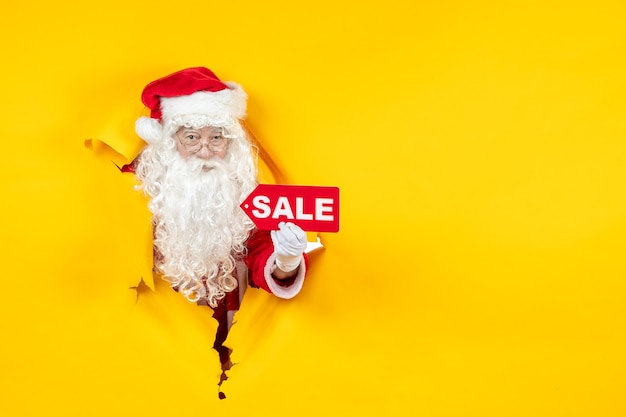 Free Photo front view of santa claus looking through ripped paper yellow wall