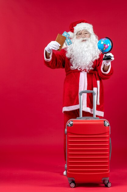 Front view of santa claus with bag holding tickets and preparing for trip on red wall