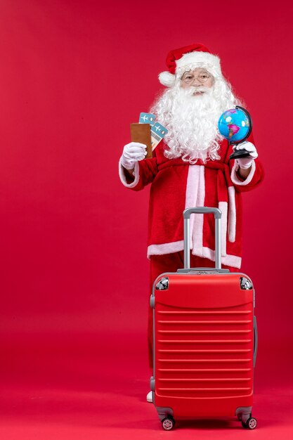 Front view of santa claus with bag holding tickets and preparing for trip on the red wall