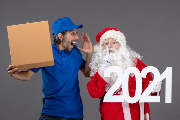 Front view of santa claus with male courier holding food box and on grey wall