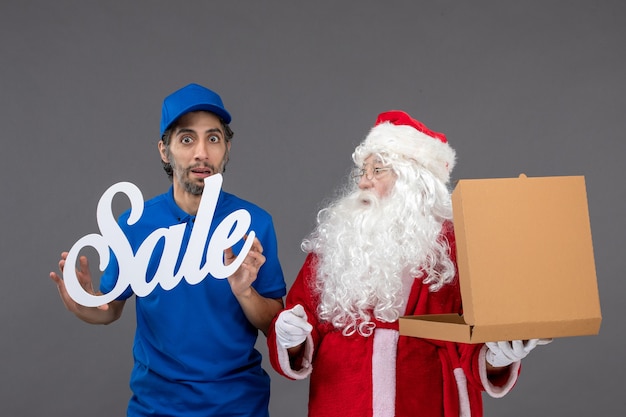 Free Photo front view of santa claus with male courier holding sale banner and food boxes on a grey wall