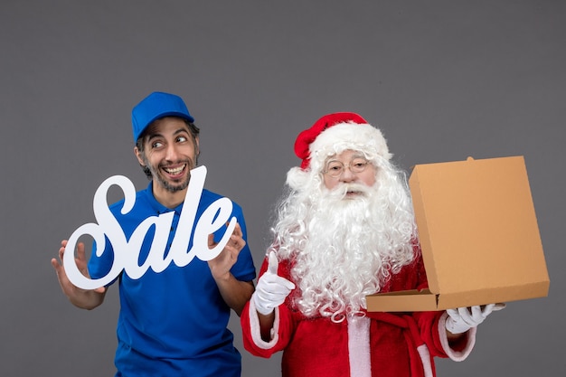 Free Photo front view of santa claus with male courier holding sale banner and food boxes on the grey wall