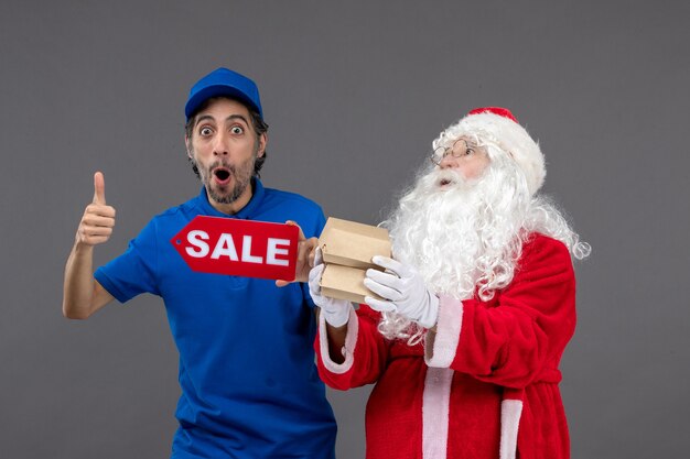 Front view of santa claus with male courier holding sale banner and food packages on grey wall