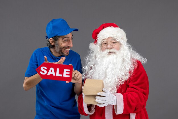 Front view of santa claus with male courier holding sale banner and food packages on grey wall