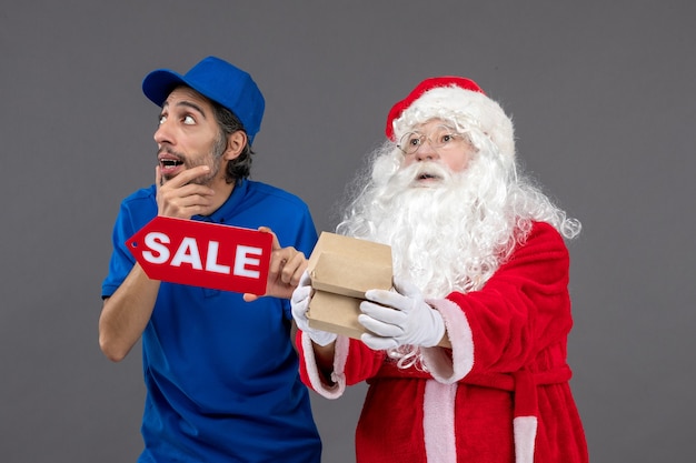 Front view of santa claus with male courier holding sale banner and food packages on grey wall