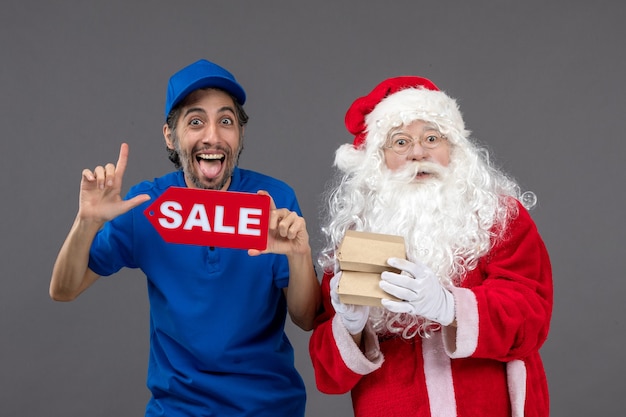 Front view of santa claus with male courier holding sale banner and food packages on grey wall