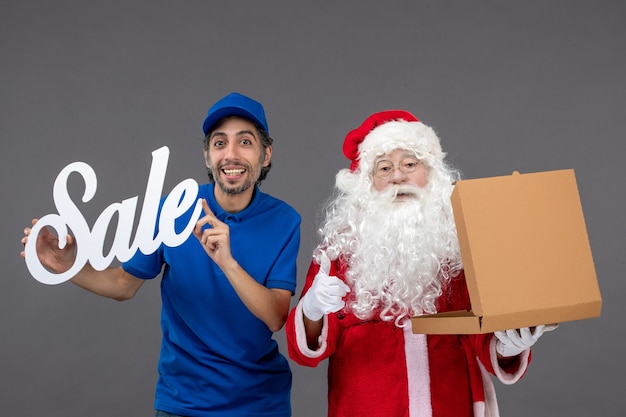 Front view of santa claus with male courier holding sale banner and opening food box on grey wall