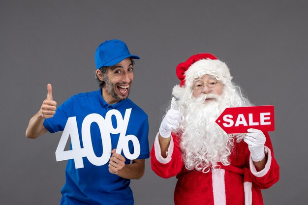 Front view of santa claus with male courier holding sale banners on a grey wall