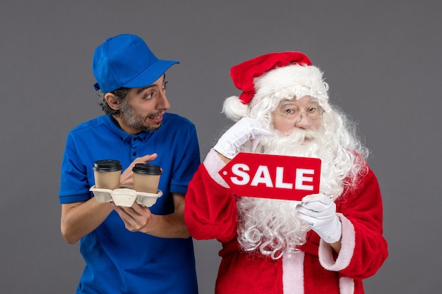 Free Photo front view of santa claus with male courier holding sale writing and coffee on grey wall