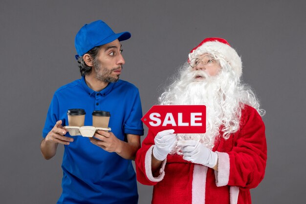 Front view of santa claus with male courier holding sale writing and coffee on grey wall